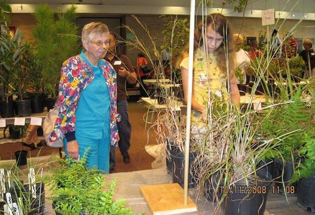 Two women looking at plants on a table at a plant sale