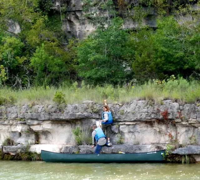 Two people climb out of a small boat onto a rocky river bank